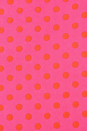 Folded hot pink fabric featuring a bold orange circular dot pattern