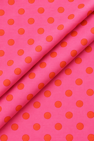 Bright pink dressmaking fabric with evenly spaced orange polka dots