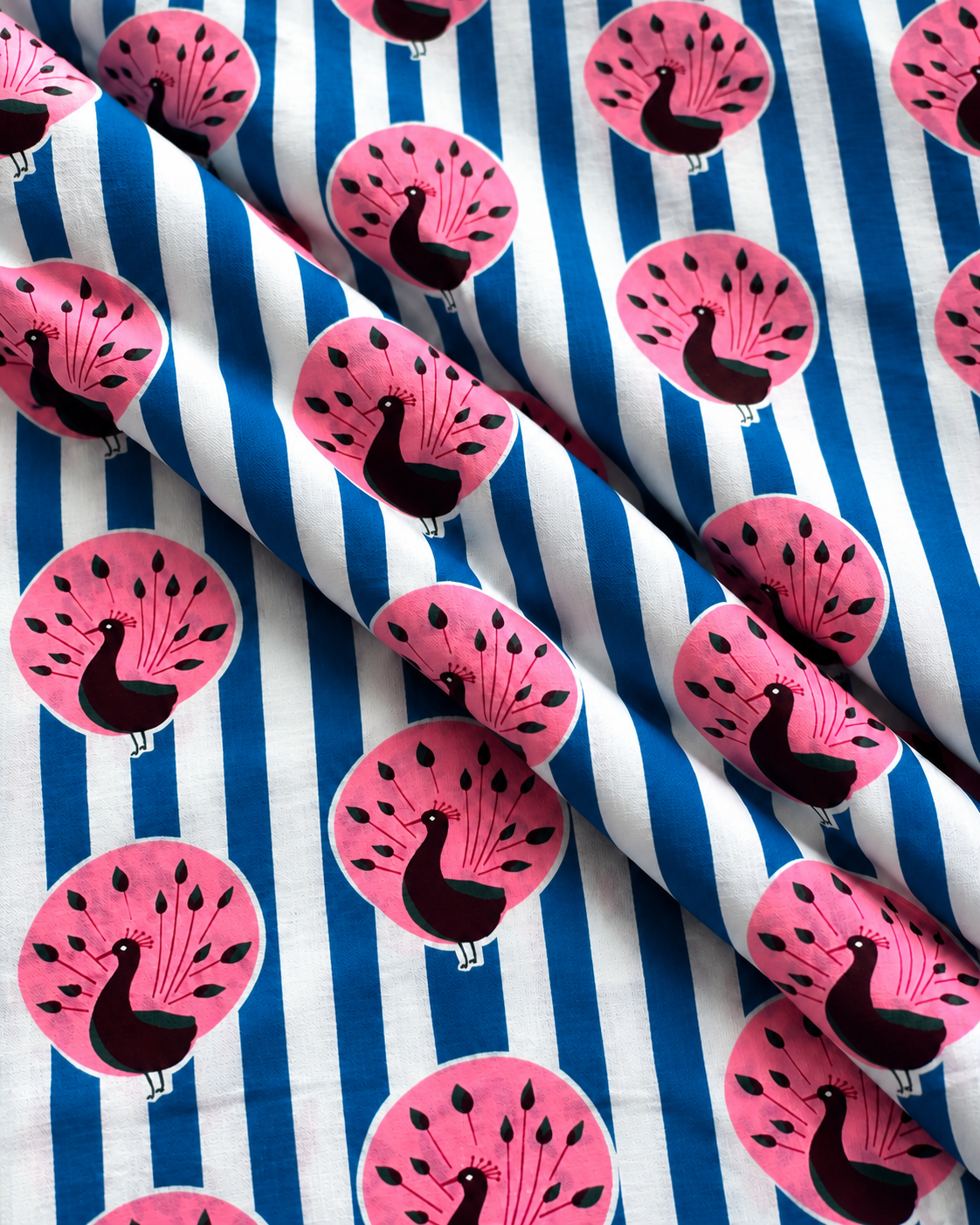 Blue white striped cotton fabric draped to show pink peacock print and natural folds