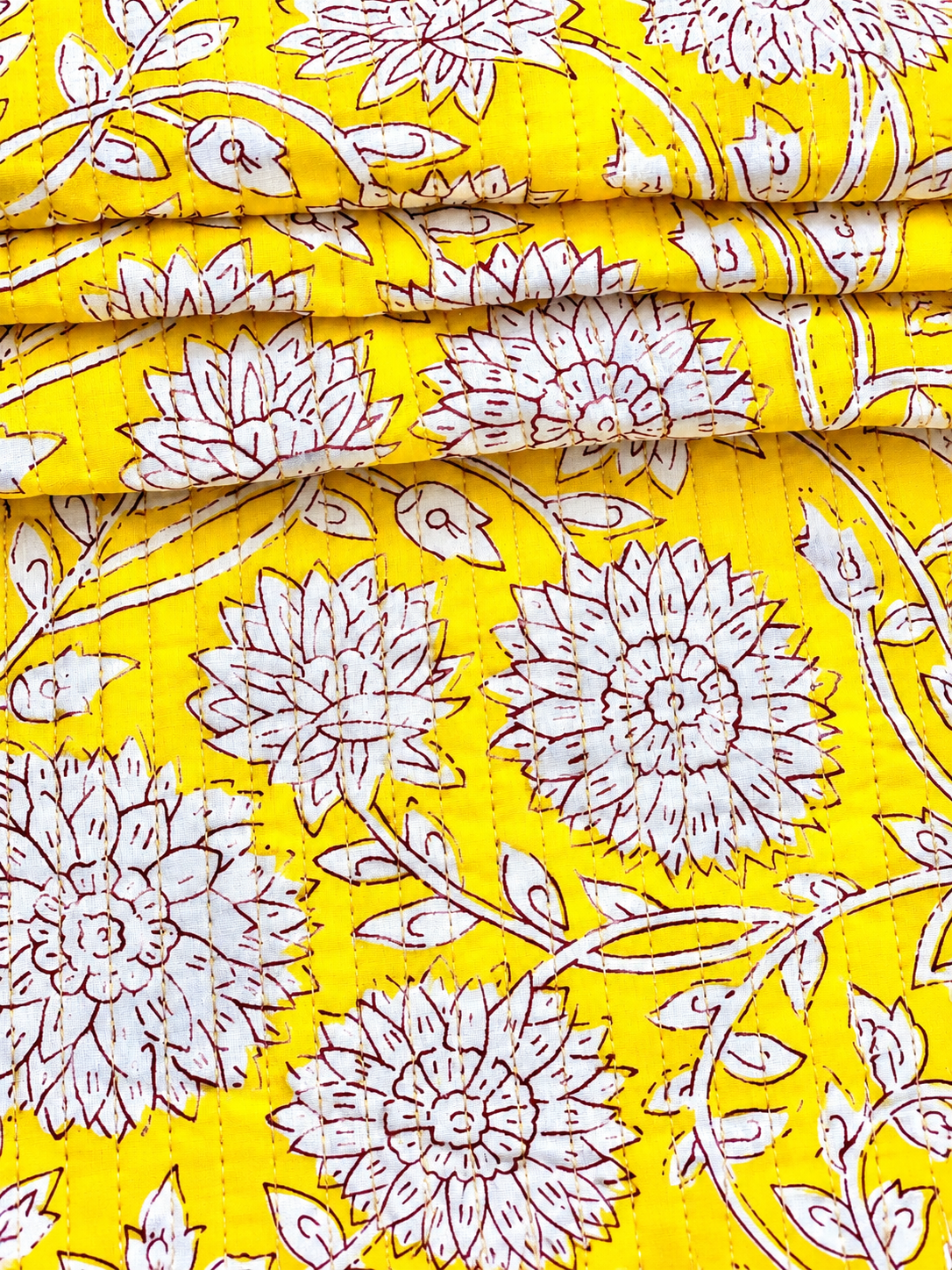White botanical flowers and leafy vines on mustard yellow quilted fabric.