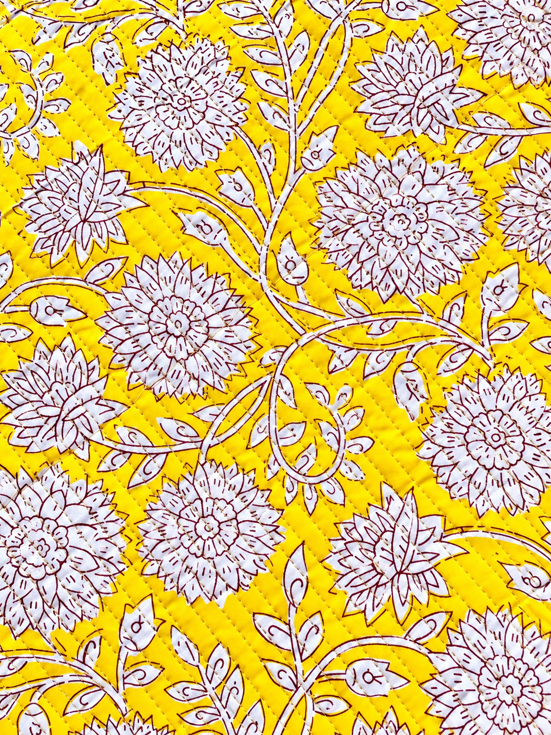 Mustard yellow quilted fabric with white floral print and burgundy outlines.