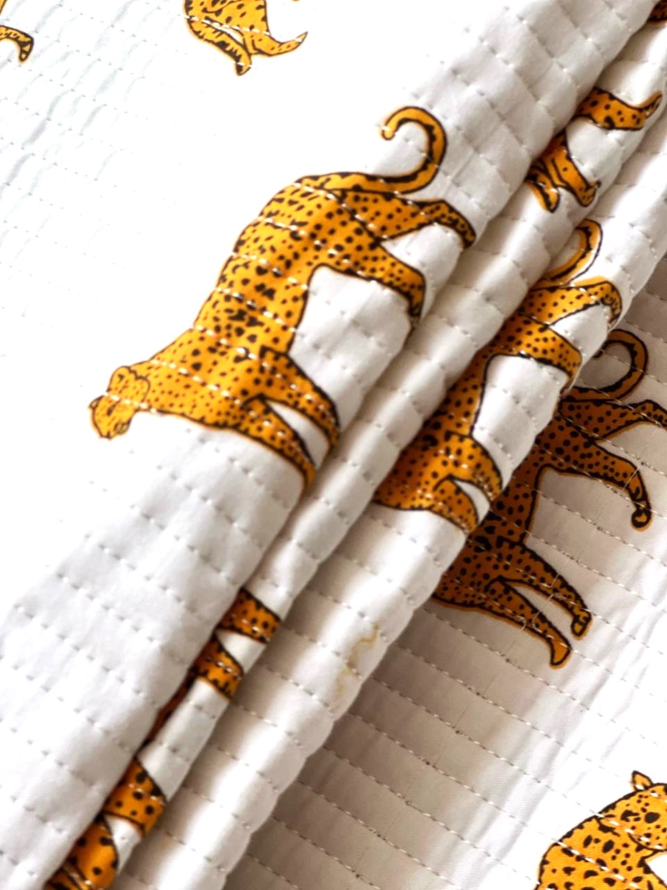 White quilted fabric featuring repeating golden leopard motifs.