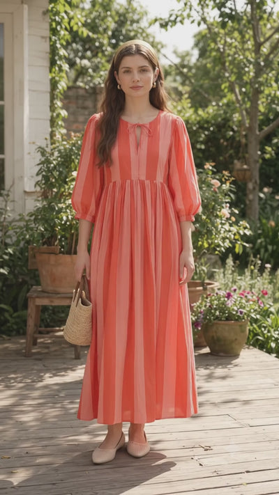 Coral and pink striped cotton maxi dress with puff sleeves worn by woman outdoors
